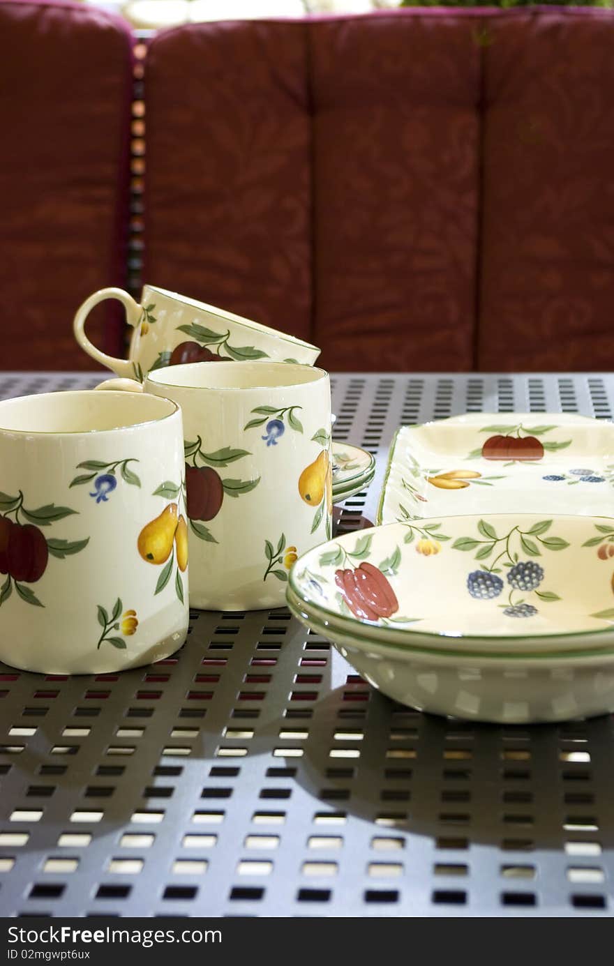 Porcelain jugs and mugs on metal table before red sofa