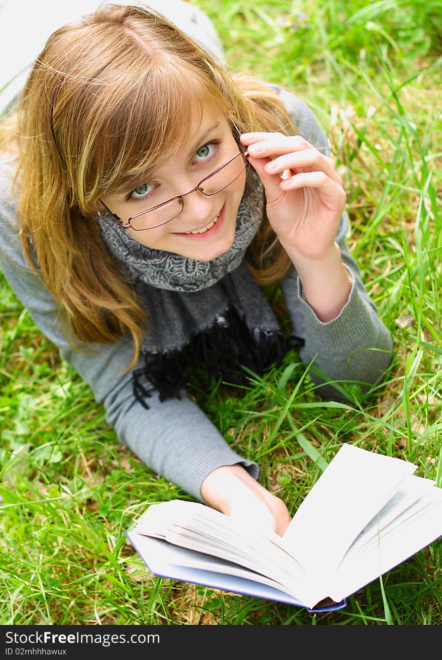 The girl lays on a green grass, and reads the book. The girl lays on a green grass, and reads the book