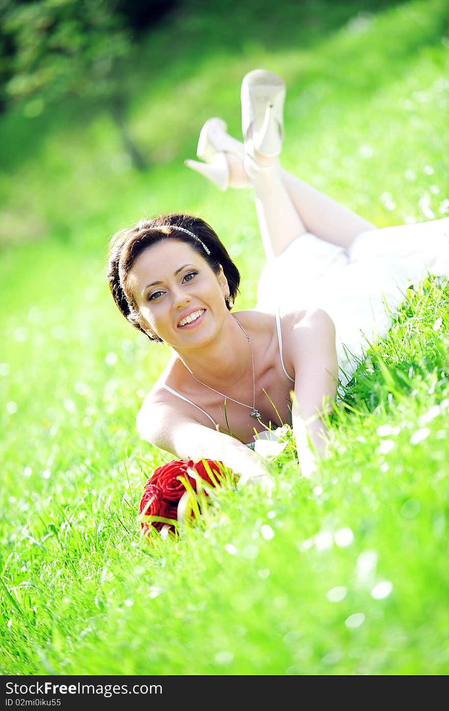 Bride in white dress lying down in  grass.