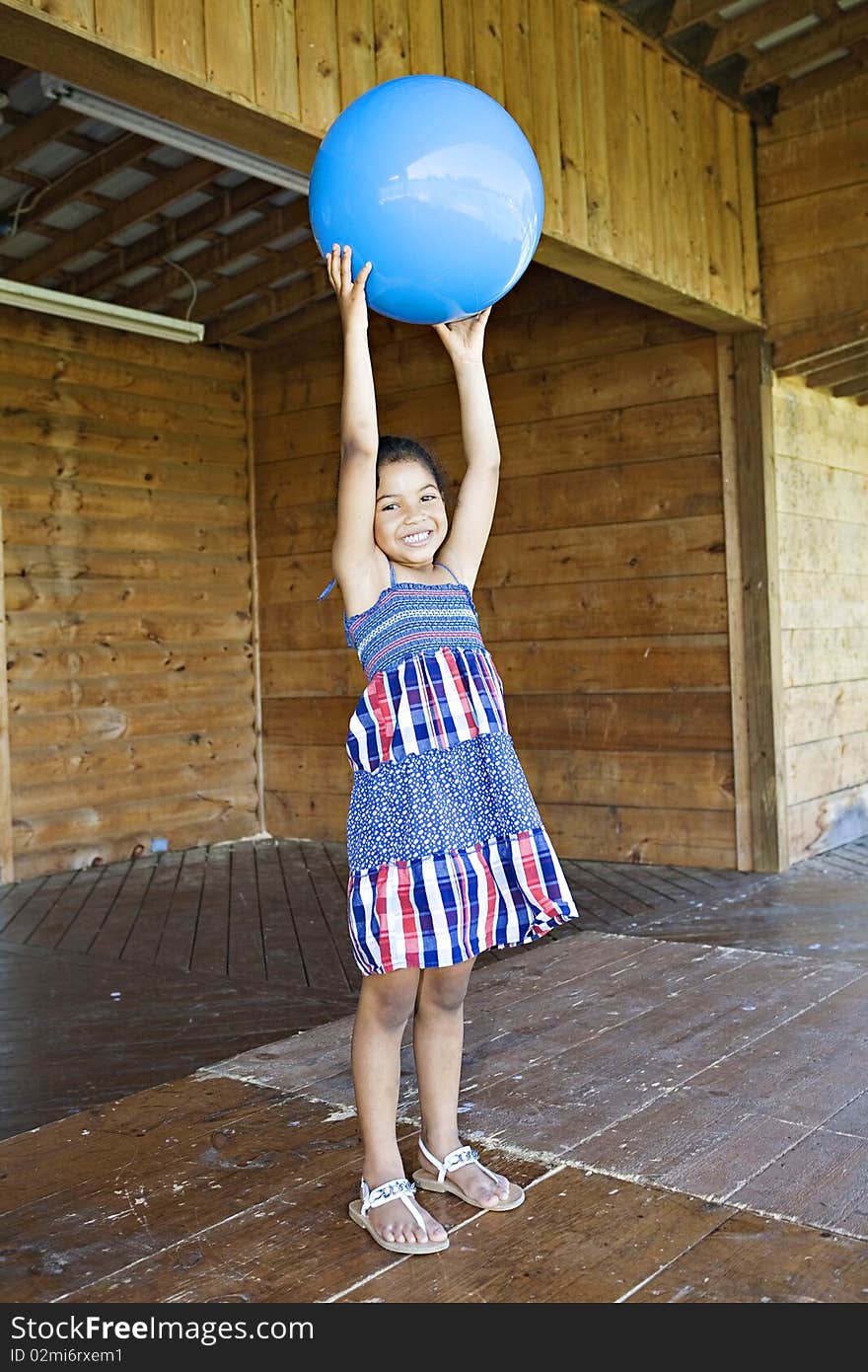 Little girl standing up, holding a big blue ball above her head, smiling. Little girl standing up, holding a big blue ball above her head, smiling