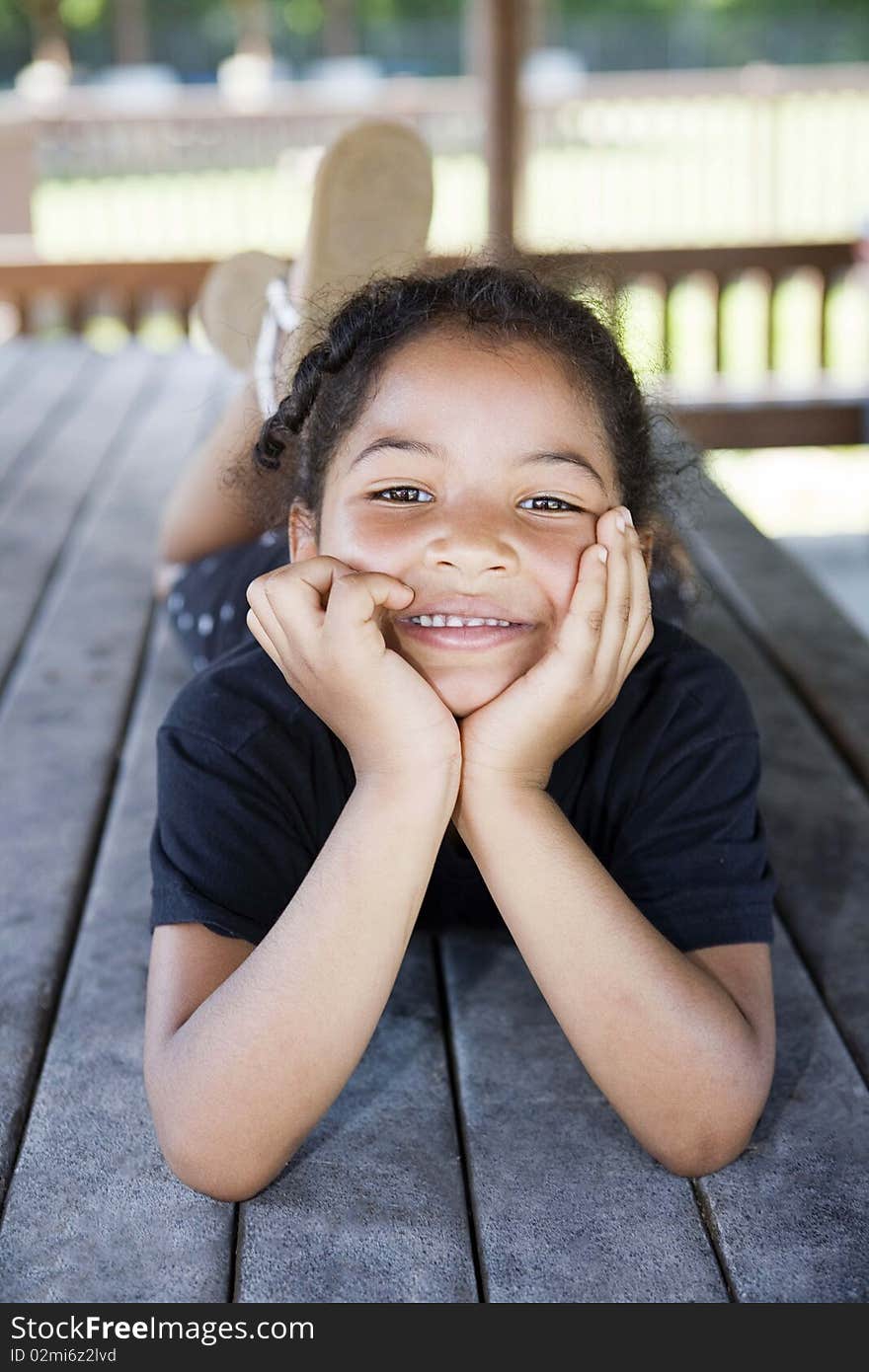 Little girl laying on a picnic table at the playground with her head cupped in her hands, smiling. Little girl laying on a picnic table at the playground with her head cupped in her hands, smiling