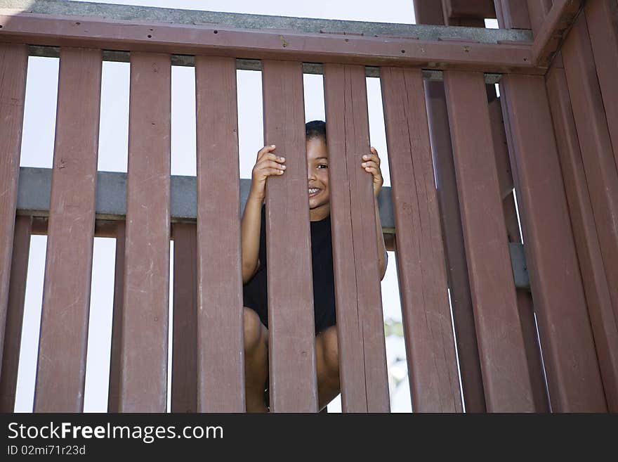 Little girl peeking between slats of a wooden fenc