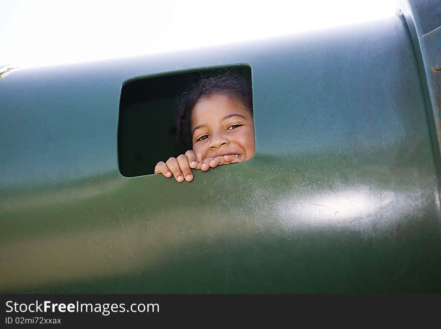 Little girl peeking through a window of a tunnel at a playground, smiling. Little girl peeking through a window of a tunnel at a playground, smiling