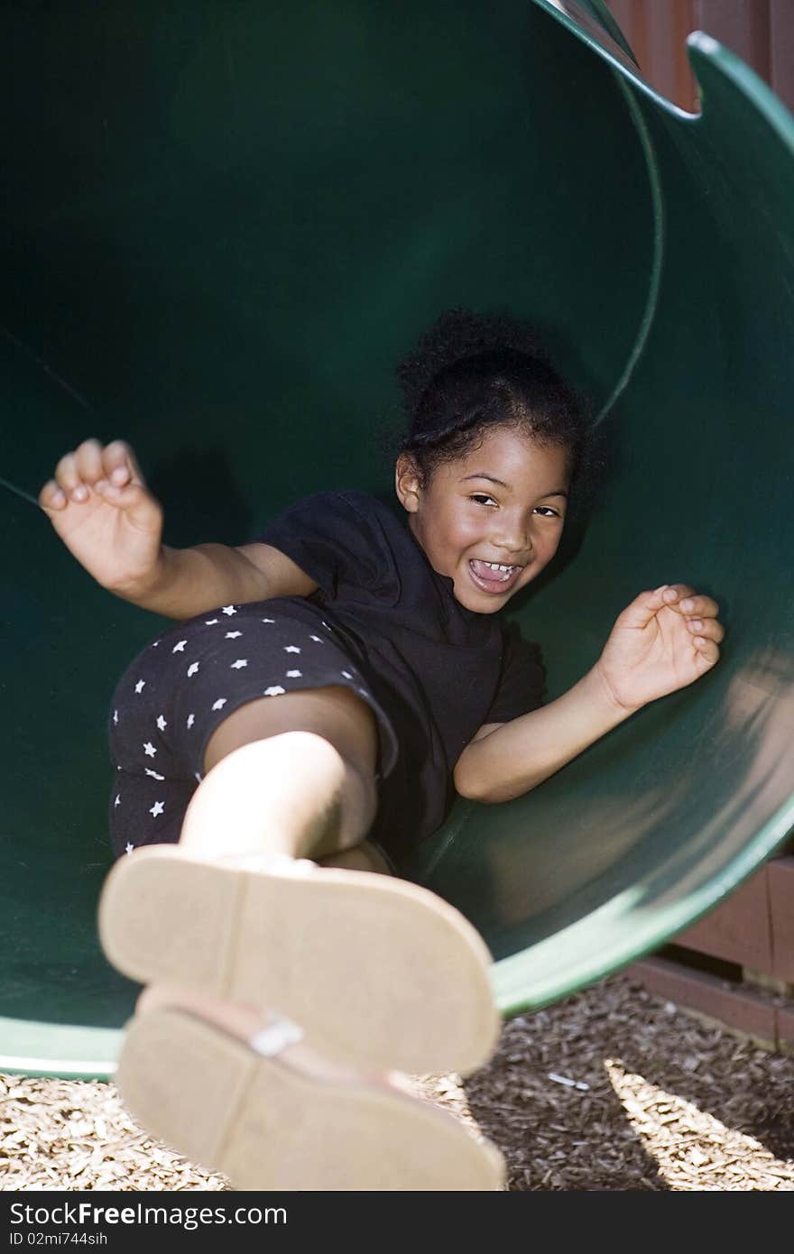 Little girl sliding down covered slide at playground. Little girl sliding down covered slide at playground
