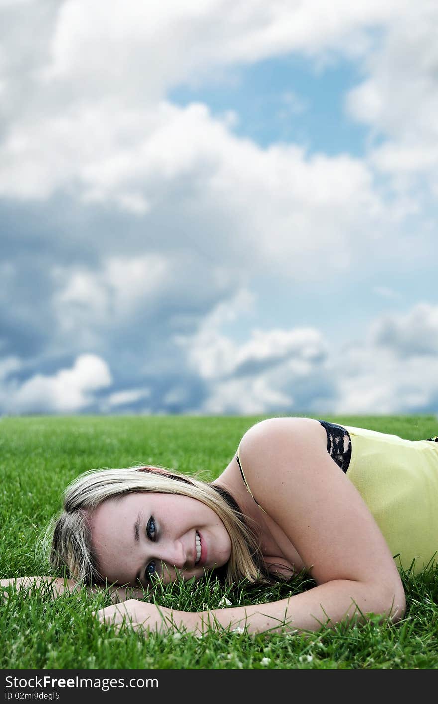 Closeup of a beautiful blond white Caucasian young adult teenage girl laying in a green grass field smiling at the camera. Closeup of a beautiful blond white Caucasian young adult teenage girl laying in a green grass field smiling at the camera.