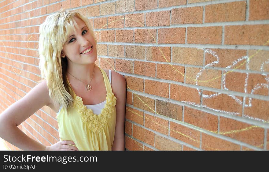 Happy young blond teenage girl standing in front of a brick wall smiling. Happy young blond teenage girl standing in front of a brick wall smiling.