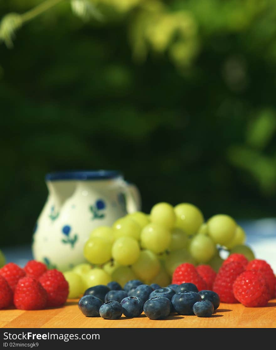 Fresh blueberries, raspberries and grapes on garden table. Focus on blueberies