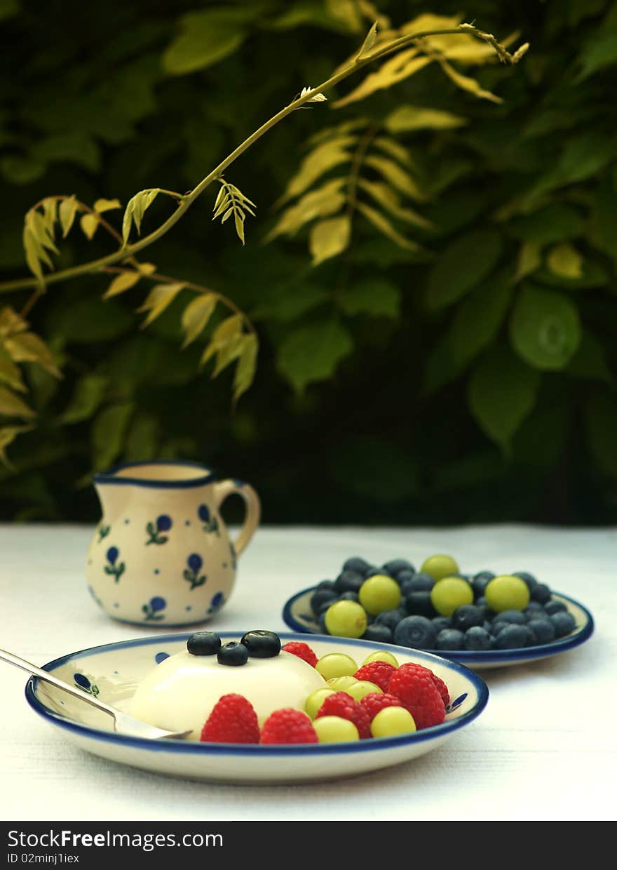 Panna cotta dessert served on garden table. Fresh blueberries, raspberries and grapes. Panna cotta dessert served on garden table. Fresh blueberries, raspberries and grapes.