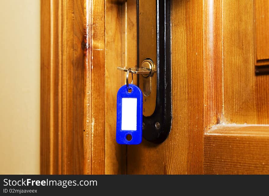 Key (with trinket for numbers) stick out in the lock of a wooden door (close up). Key (with trinket for numbers) stick out in the lock of a wooden door (close up)