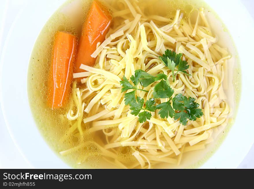 Chicken soup with macaroni and carrots decorated with parsley on a plate