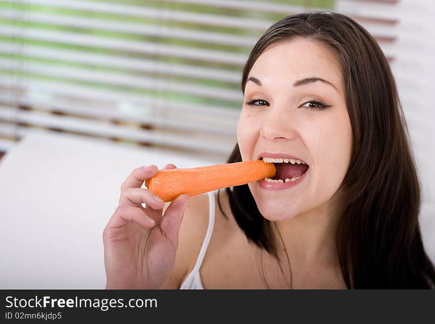 Young attractive brunette woman with carrot in bed. Young attractive brunette woman with carrot in bed