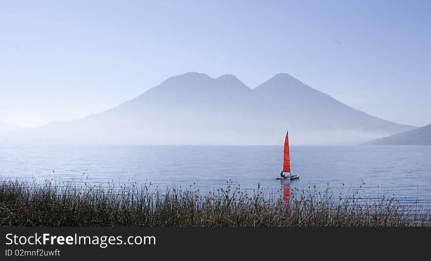 Morning fog is covered vulcan near the lake. sailboat on water. Blue tones.