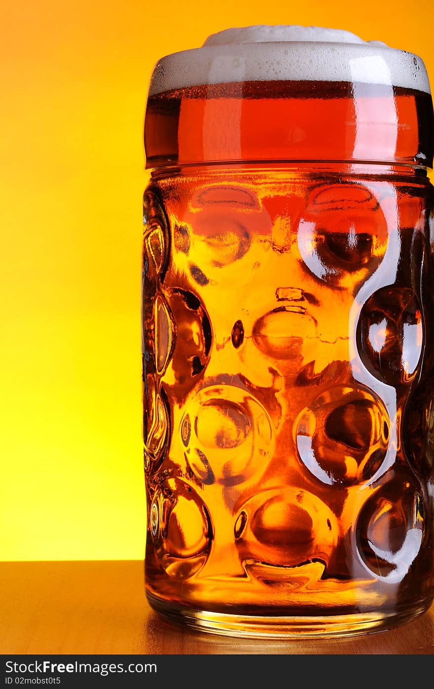 Mug of cold beer on yellow background