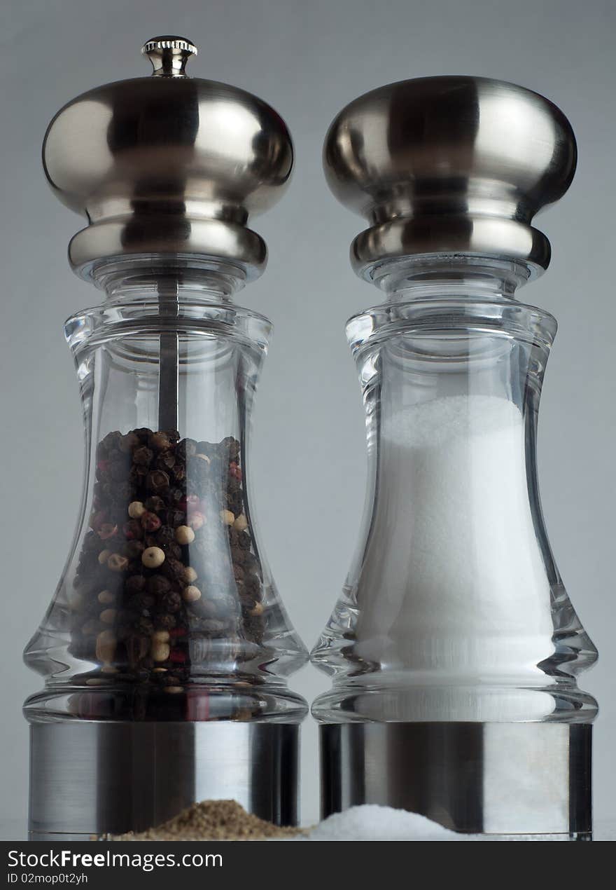 An in focus salt and pepper shaker behind a pile of the spices. An in focus salt and pepper shaker behind a pile of the spices.