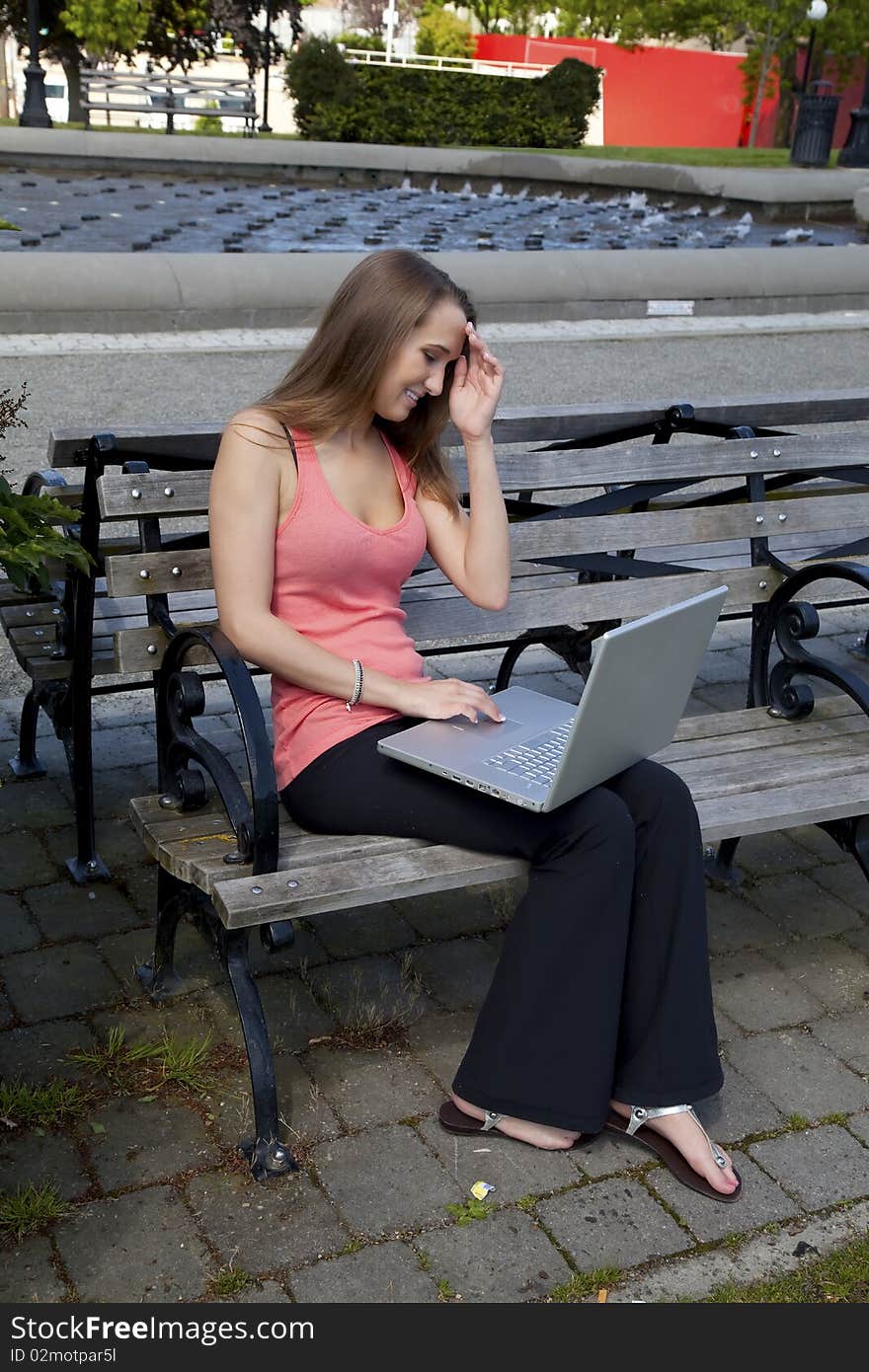 A student sitting on a park bench trying to think of what to do on her computer while she is relaxing at the park. A student sitting on a park bench trying to think of what to do on her computer while she is relaxing at the park.