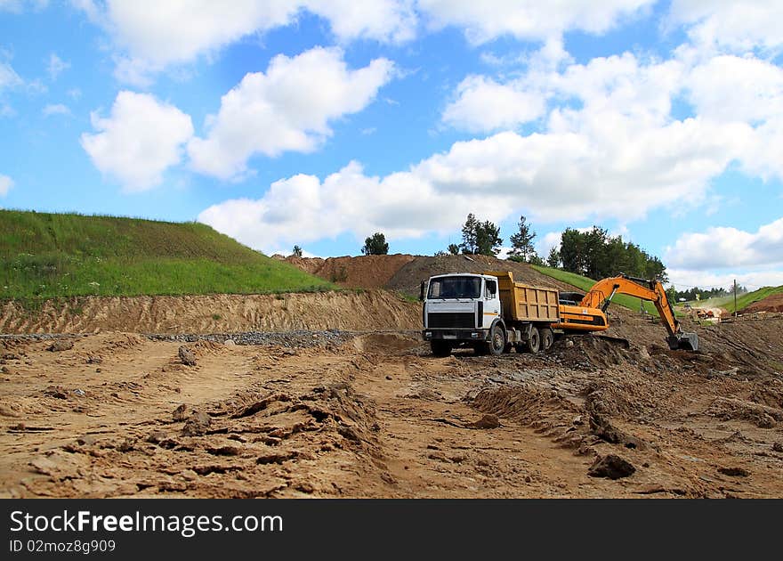 Excavator loading truck shot against the background of the pit and blue sky. Excavator loading truck shot against the background of the pit and blue sky