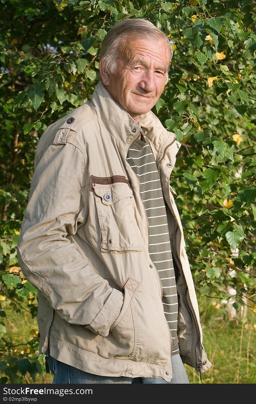 Portrait of the grey-haired elderly man in a beige jacket in village on the nature. Portrait of the grey-haired elderly man in a beige jacket in village on the nature