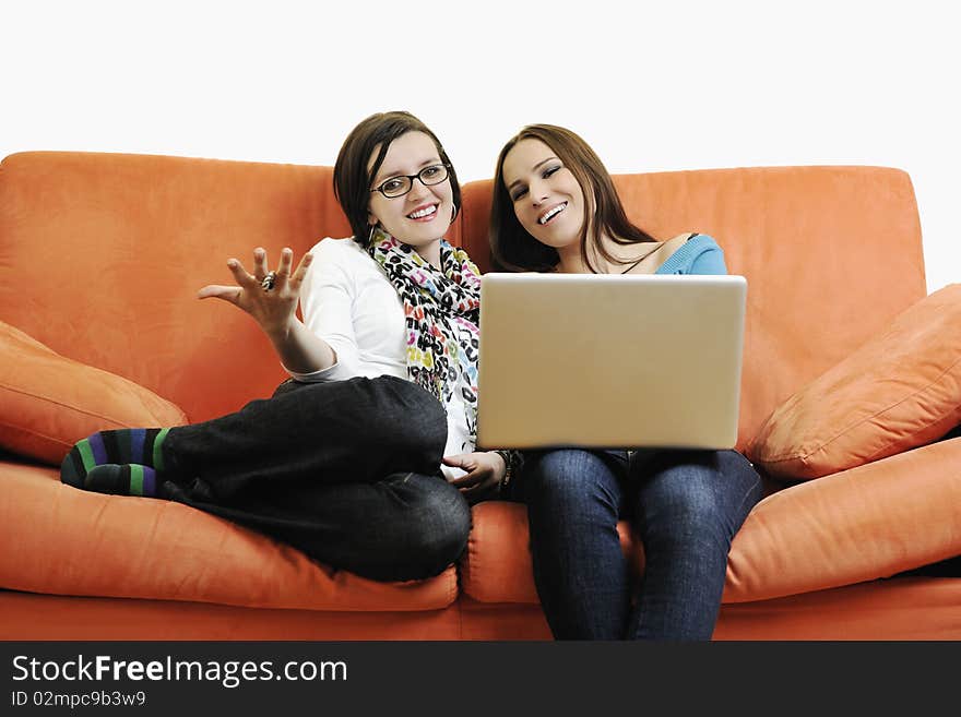 Two happy young woman working on laptop computer on red sofa isolated on white. Two happy young woman working on laptop computer on red sofa isolated on white