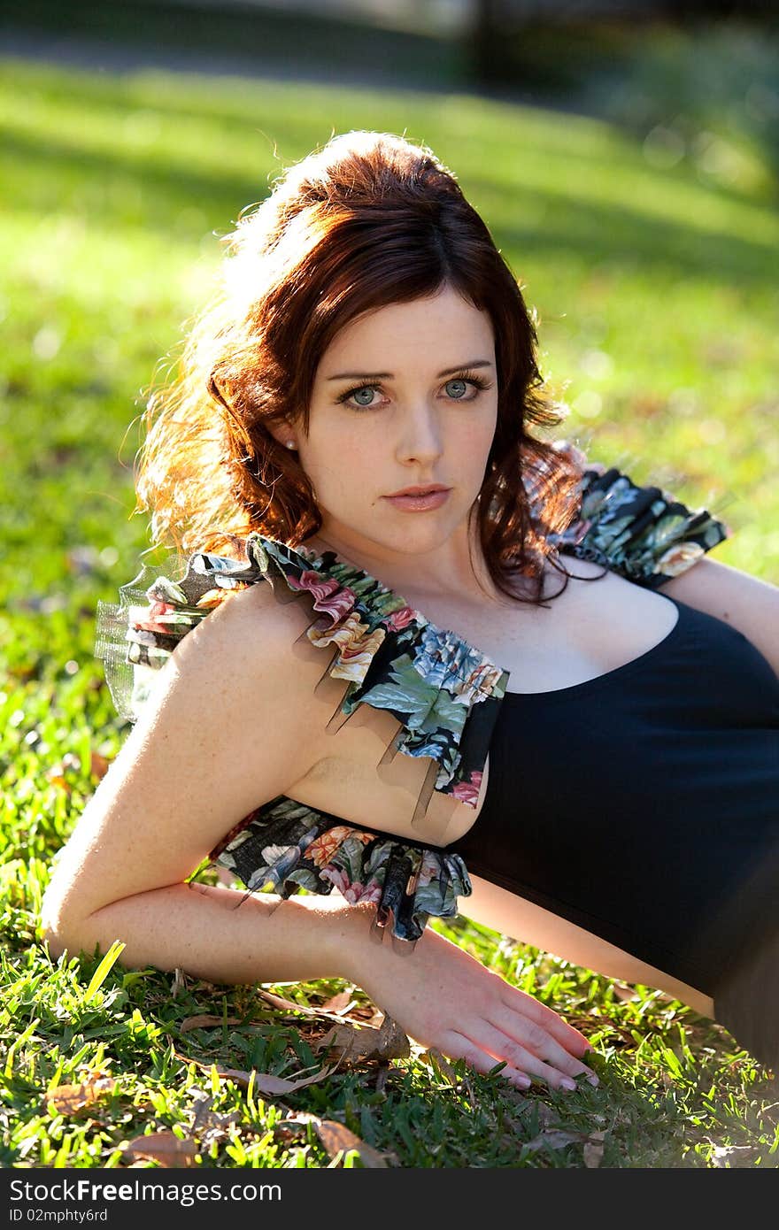 Beautiful young woman is lying down on the grass and looking at the camera. Vertical shot. Beautiful young woman is lying down on the grass and looking at the camera. Vertical shot.