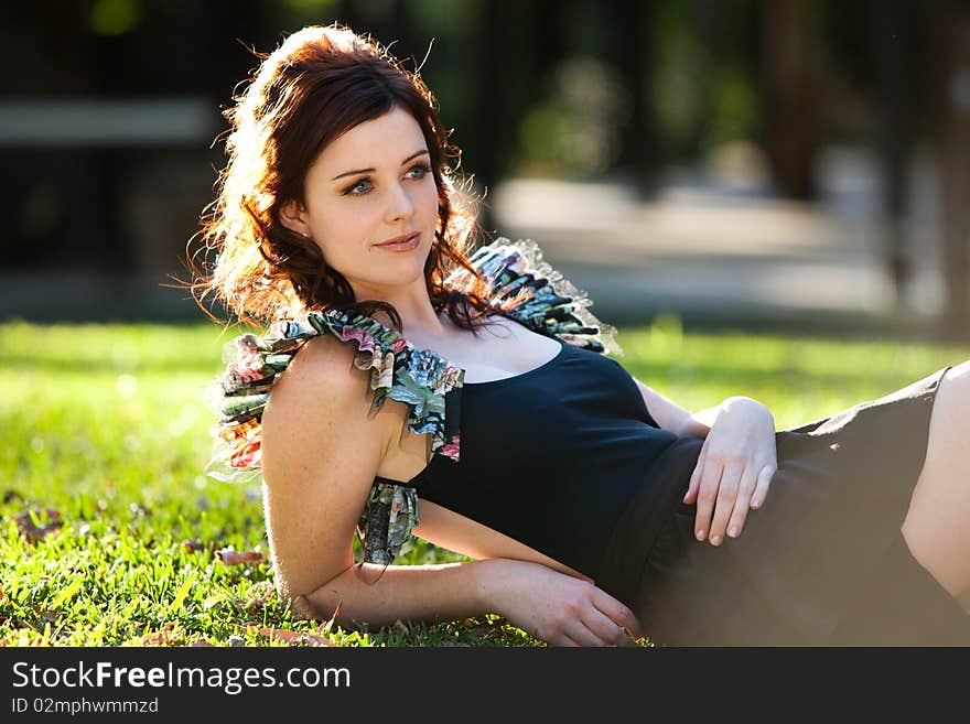 Beautiful young woman is lying down on the grass and smiling to the side. Horizontal shot. Beautiful young woman is lying down on the grass and smiling to the side. Horizontal shot.