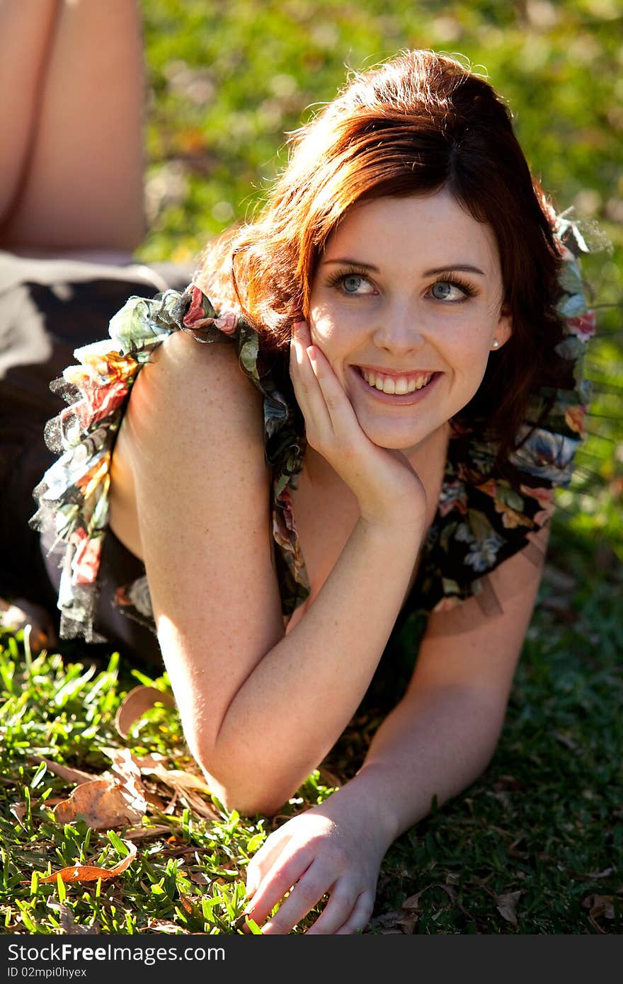 Beautiful young woman is lying on the grass and smiling to the side. Vertical shot. Beautiful young woman is lying on the grass and smiling to the side. Vertical shot.