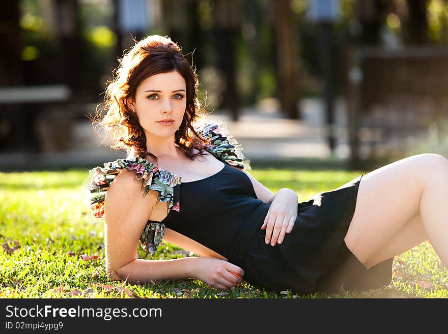 Beautiful young woman is lying down on the grass and looking at the camera. Horizontal shot. Beautiful young woman is lying down on the grass and looking at the camera. Horizontal shot.