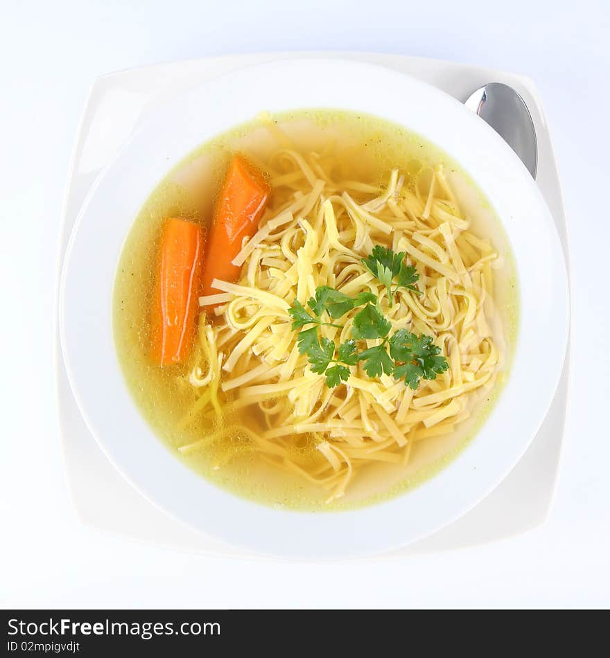 Chicken soup with macaroni and carrots decorated with parsley on a plate with a spoon