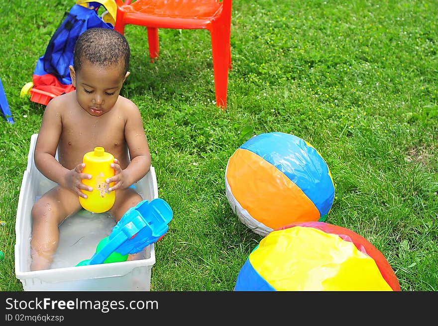 Young child playing outside in small pool of water with beechballs around. Young child playing outside in small pool of water with beechballs around