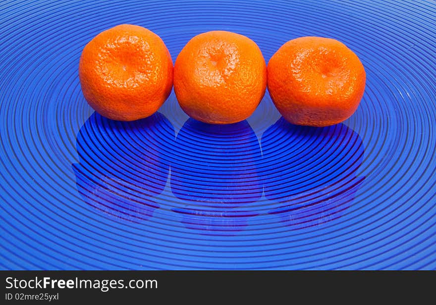 Three tangerines in row on blue glass plate