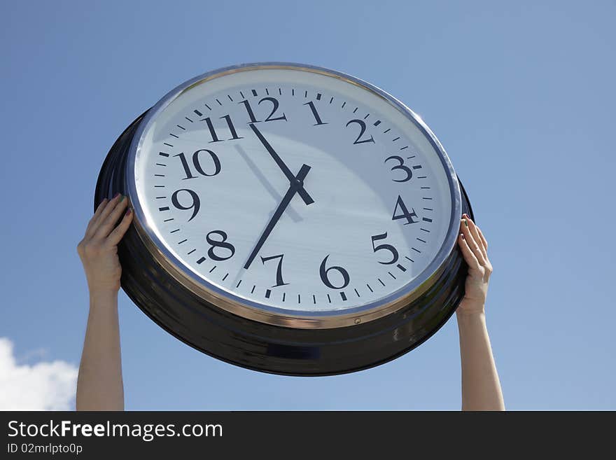 Hands lifting a big clock outdoors on a summer day. Blue sky background. Hands lifting a big clock outdoors on a summer day. Blue sky background.