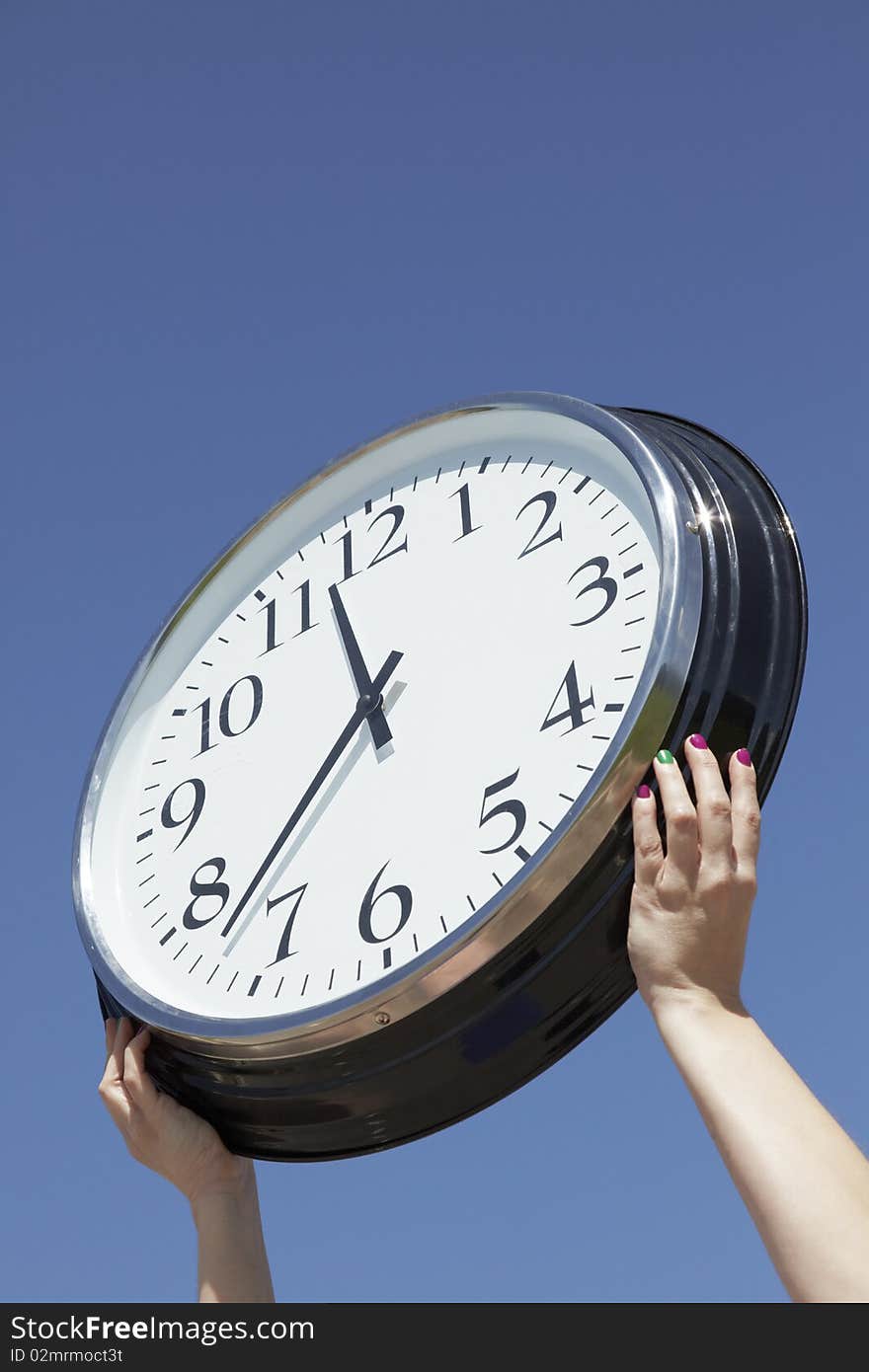 Hands lifting a big clock outdoors on a summer day. Blue sky background. Hands lifting a big clock outdoors on a summer day. Blue sky background.