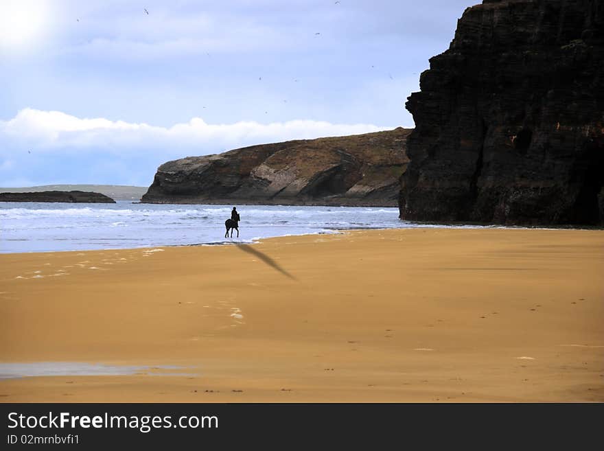 Silhouette of a horse and rider galloping on ballybunion beach with cliffs at sunset in kerry ireland. Silhouette of a horse and rider galloping on ballybunion beach with cliffs at sunset in kerry ireland