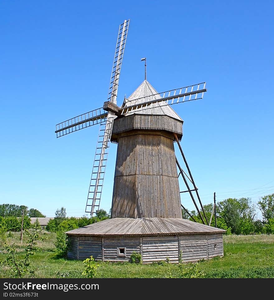 On the green grass, the wooden windmill against the blue sky.