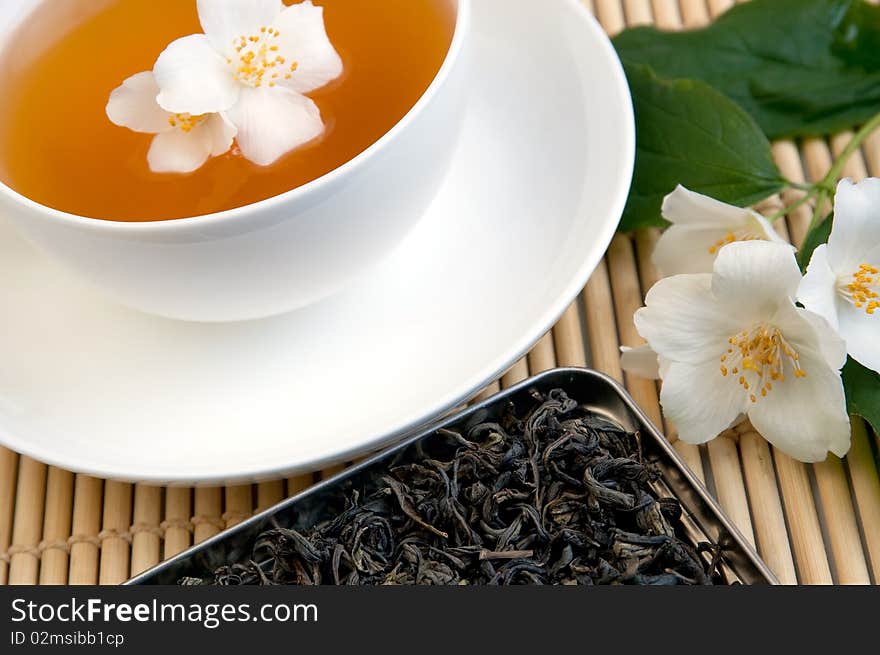 A cup of tea on a tray with dried tea and jasmine branch. A cup of tea on a tray with dried tea and jasmine branch