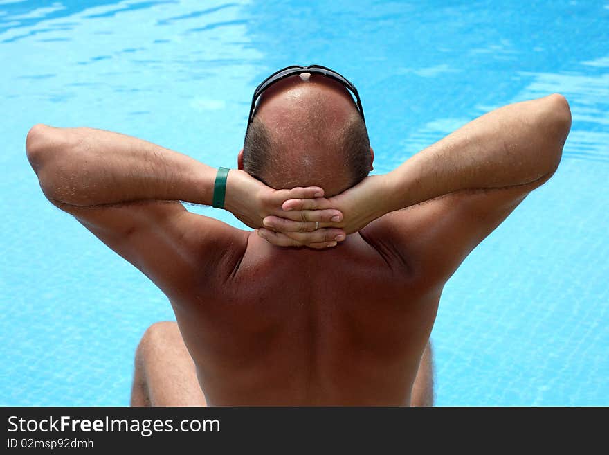 Man sitting near the pool and sunbathe, back