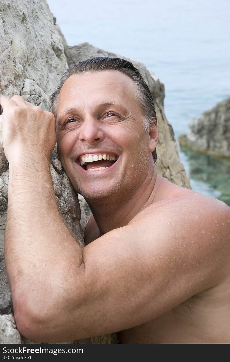 A color portrait photo of a happy mature man laughing as he leans against a rock at the beach. A color portrait photo of a happy mature man laughing as he leans against a rock at the beach.