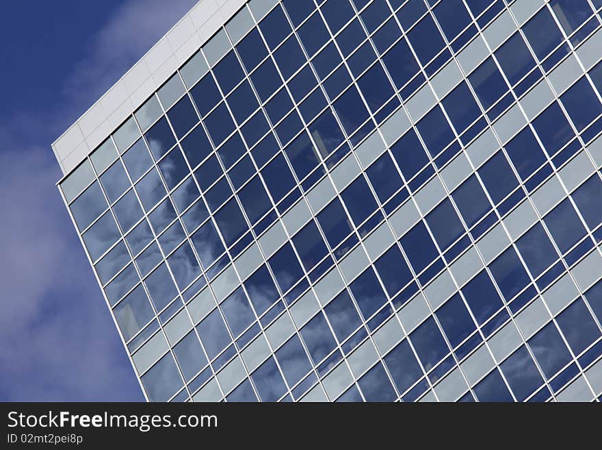 Tilted shot looking up at a modern office building. Puffy clouds reflected in windows. Horizontal shot. Tilted shot looking up at a modern office building. Puffy clouds reflected in windows. Horizontal shot.