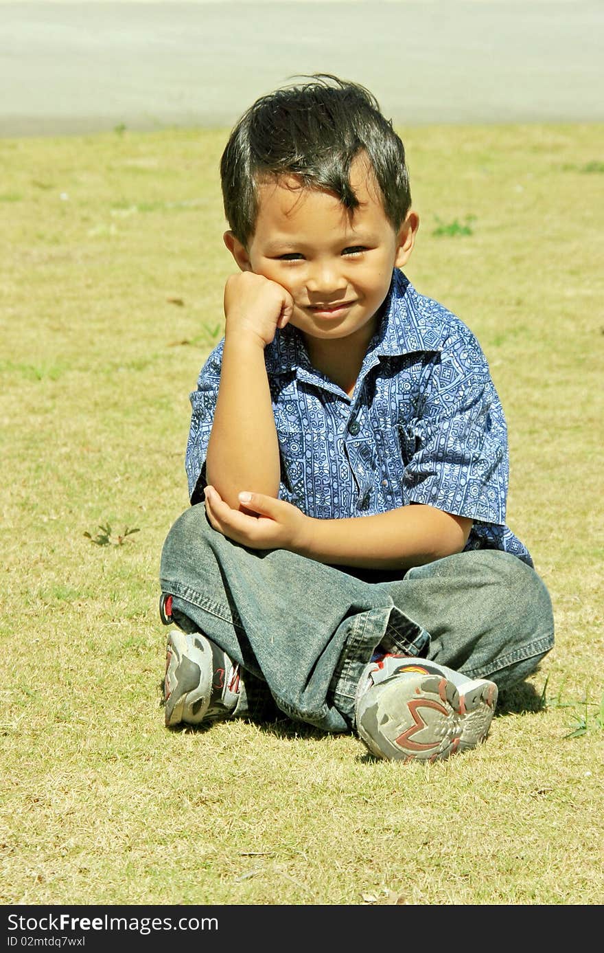 An Asian young boy setting in the grass land. An Asian young boy setting in the grass land