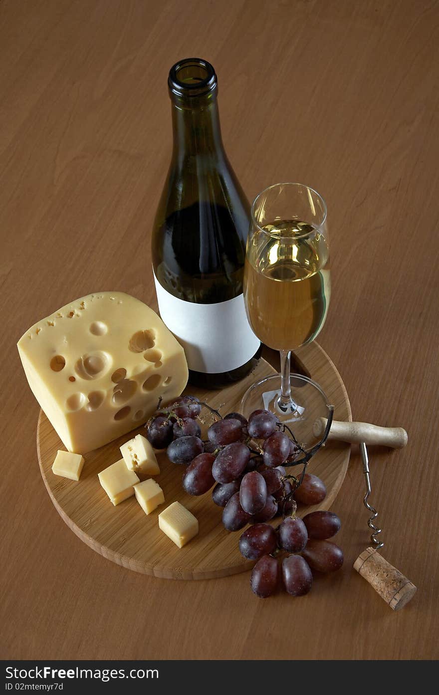 Bottle and glass of white wine with cheese, grapes, a cork and a corkscrew on a wood background