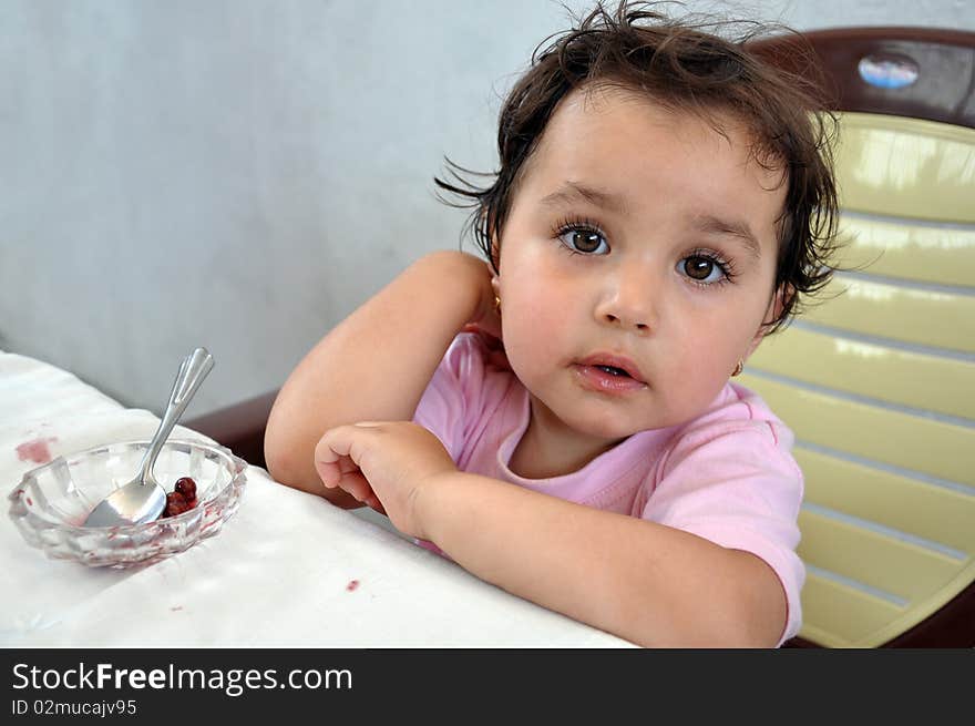 A little girl with lips dirty with jam sitting near an empty saucer. A little girl with lips dirty with jam sitting near an empty saucer