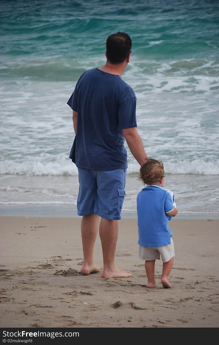 A father and son looking out at the ocean and the waves and they are both dressed in blue. A father and son looking out at the ocean and the waves and they are both dressed in blue.