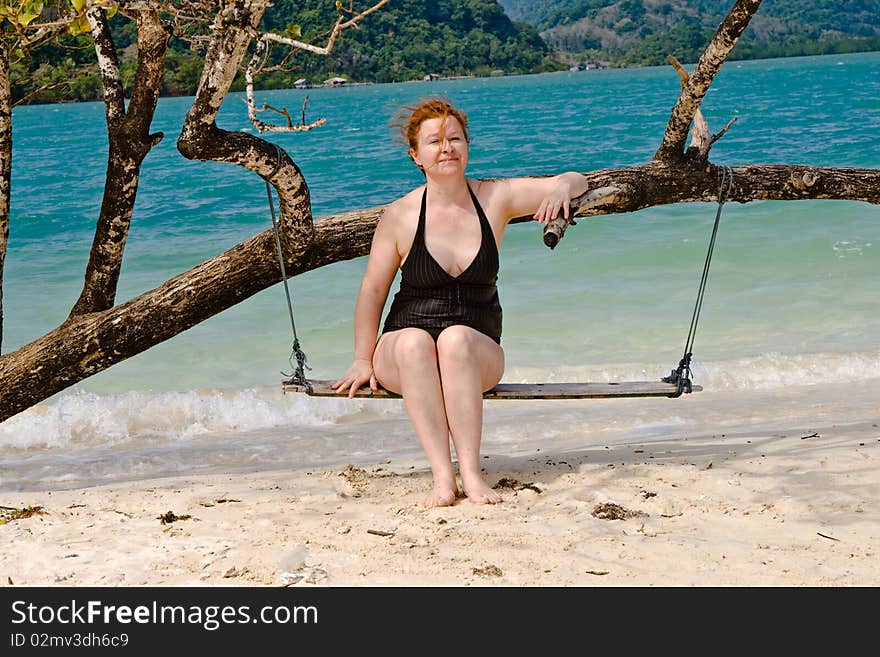 Happy woman sitting on a swing, relaxing on a idyllic beach like paradise