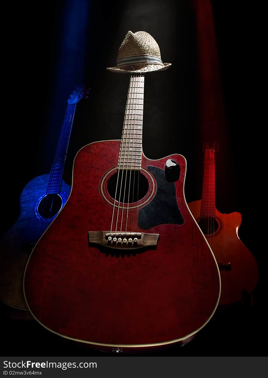 Three acoustic guitars on the stage lit with the overhead lights , against black background, useful for music and entertainment themes