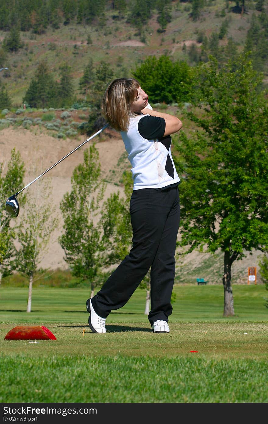 Blond female golfer following her ball from the tee-box