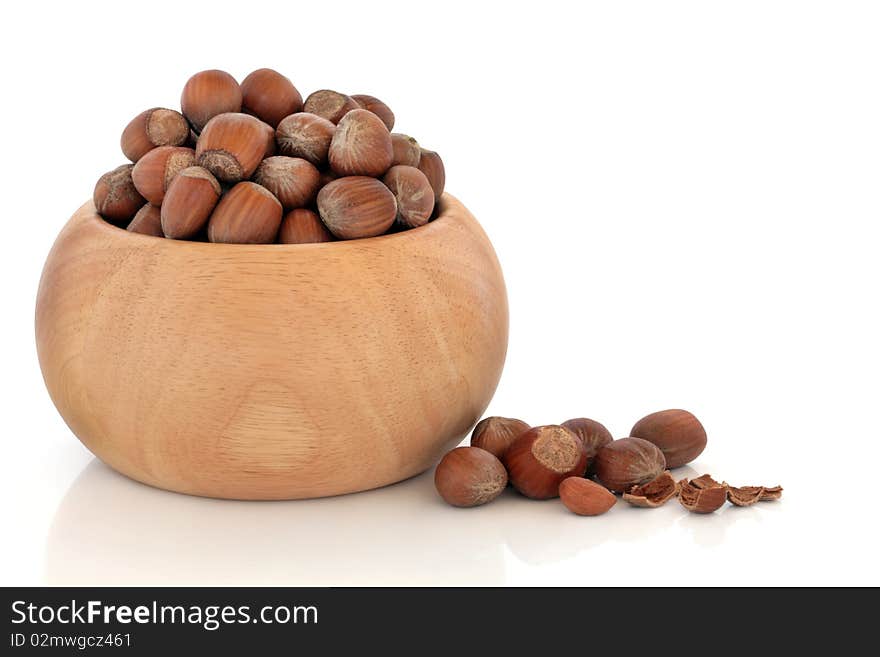 Hazelnuts in a beech wood bowl and scattered, isolated over white background with reflection.