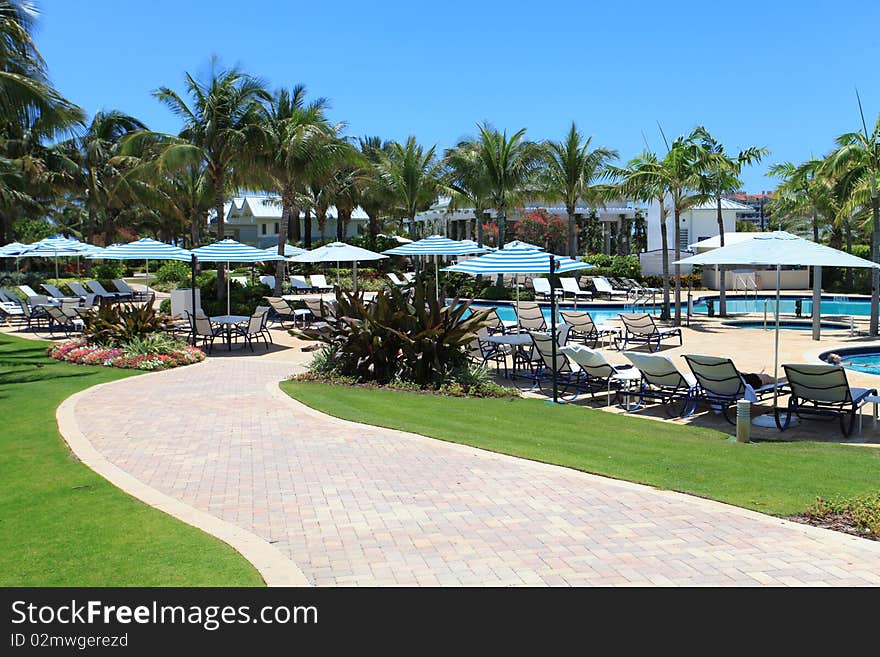 Stone pathyway leading to a large luxury pool with umbrellas.