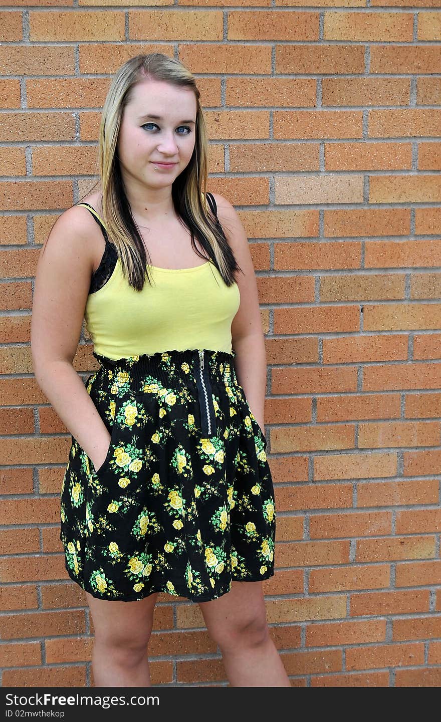 Happy young blond teenage girl standing in front of a brick wall smiling. Happy young blond teenage girl standing in front of a brick wall smiling.