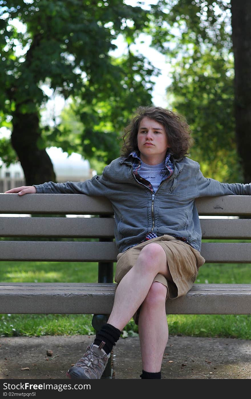 Young white Caucasian teenager sits on a bench in a public park, relaxing while he thinks things over. Young white Caucasian teenager sits on a bench in a public park, relaxing while he thinks things over.