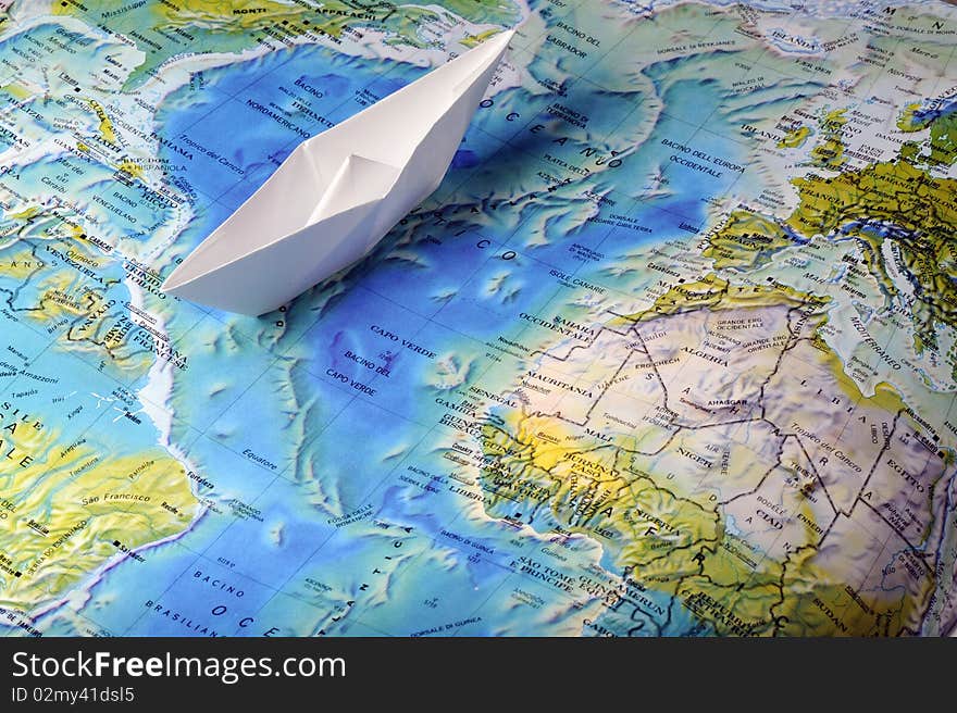 A white toy paperboat on a map. A white toy paperboat on a map.