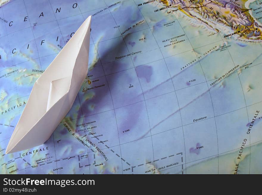 A white toy paperboat on a map. A white toy paperboat on a map.